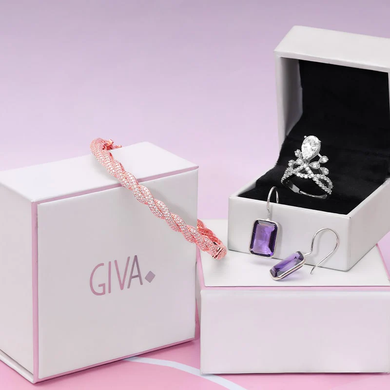 A GIVA gift box with a rose-gold bracelet, a silver ring set with a pear-cut stone, and amethyst drop earrings, on a soft-pink background