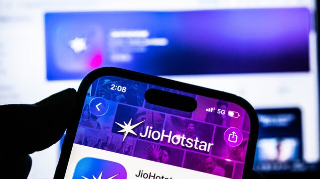 A hand holding a phone showing the JioHotstar splash