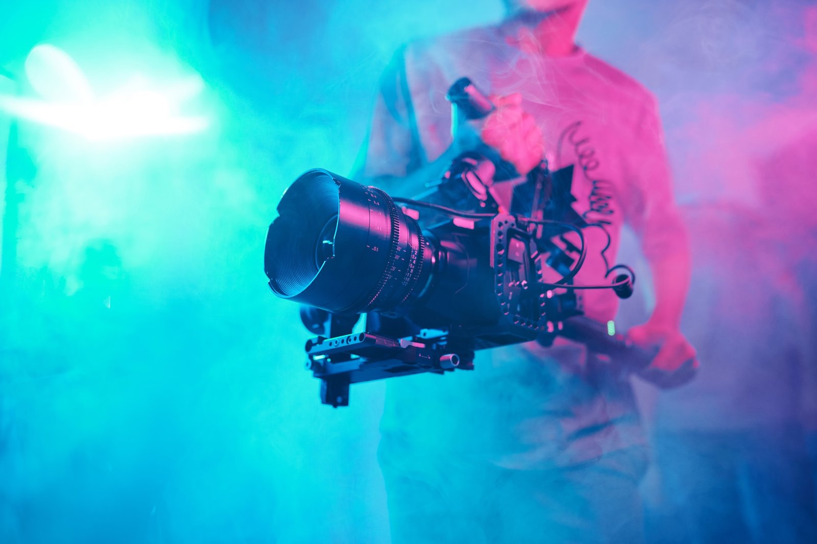 A cinematographer holding a cinema camera against a neon-blue and pink haze — the on-location half of the film that no AI tool touches