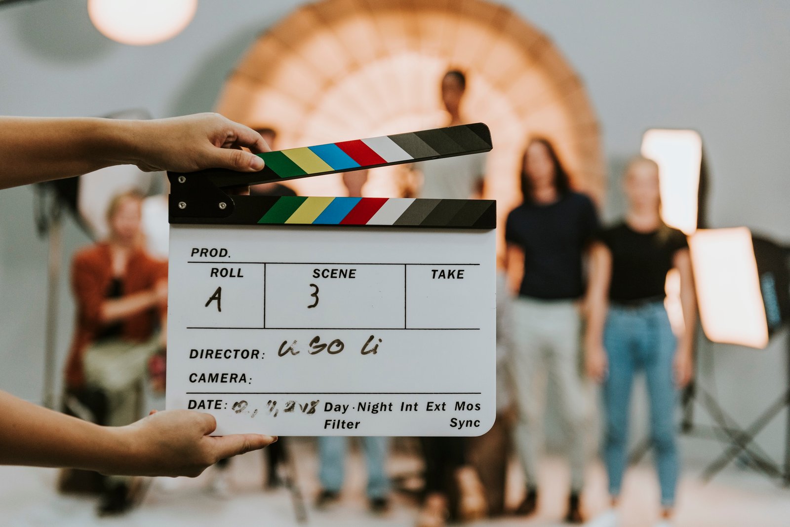 A clapperboard held up in front of a film set with production crew visible behind